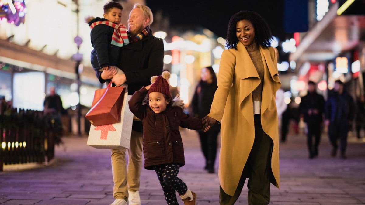 A front-view shot of a multi-ethnic family with two children walking down a city street on a cold December night.