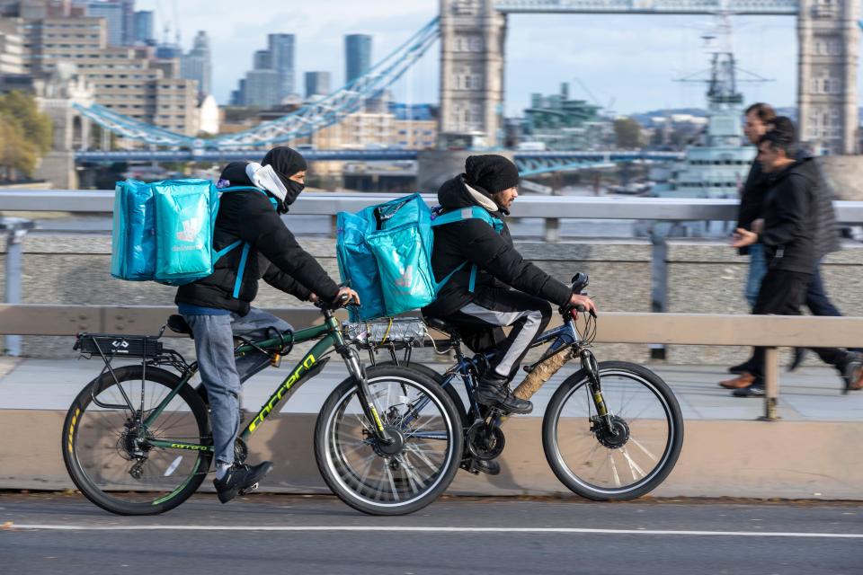 A deliveroo cycle courier riding an e-bike across, London Bridge, London, UK.  17 Nov 2022