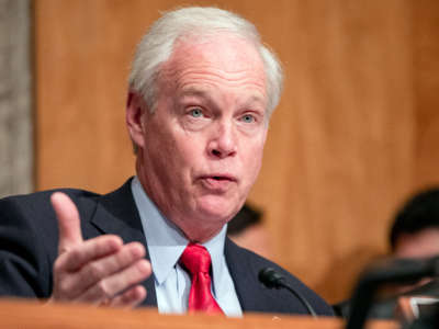 Sen. Ron Johnson, right hand raised outward, speaks into a microphone at a hearing at the U.S. Capitol