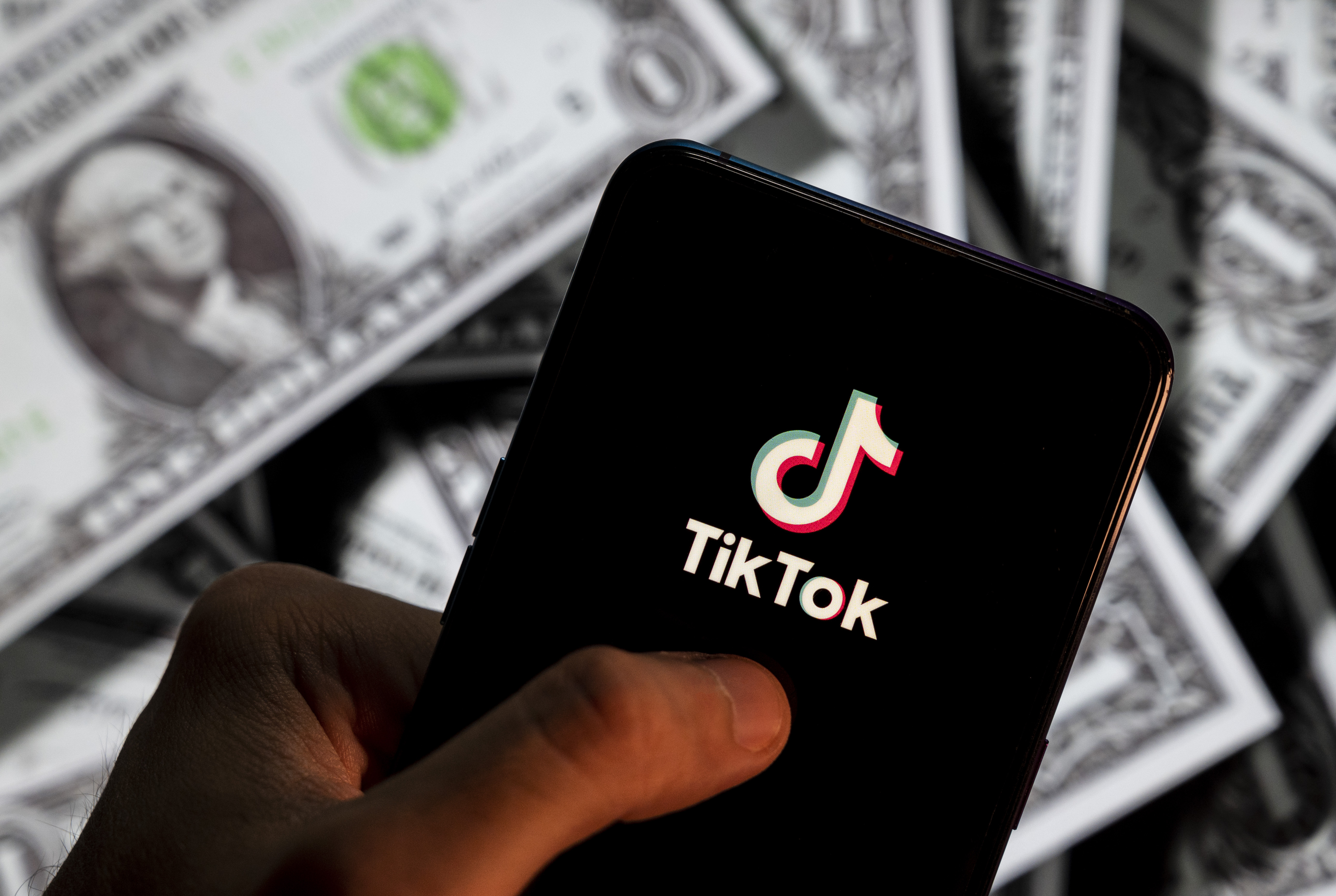 In this photo illustration, a TikTok logo seen displayed on a smartphone with USD (United States dollar) currency in the background.