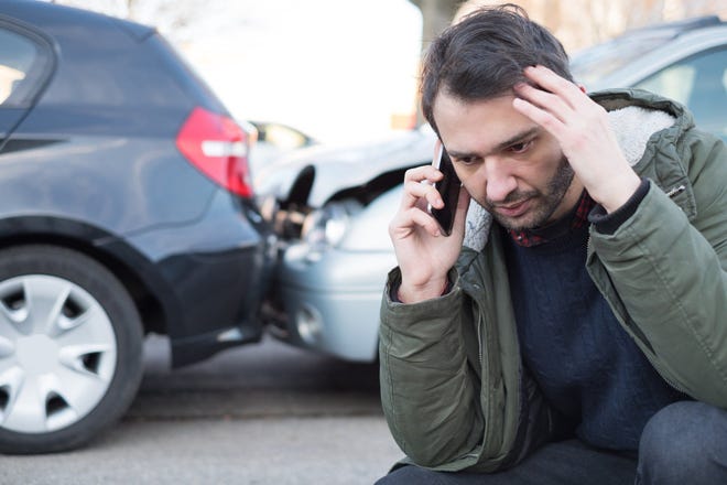 Person on the phone in front of  two cars with damage.