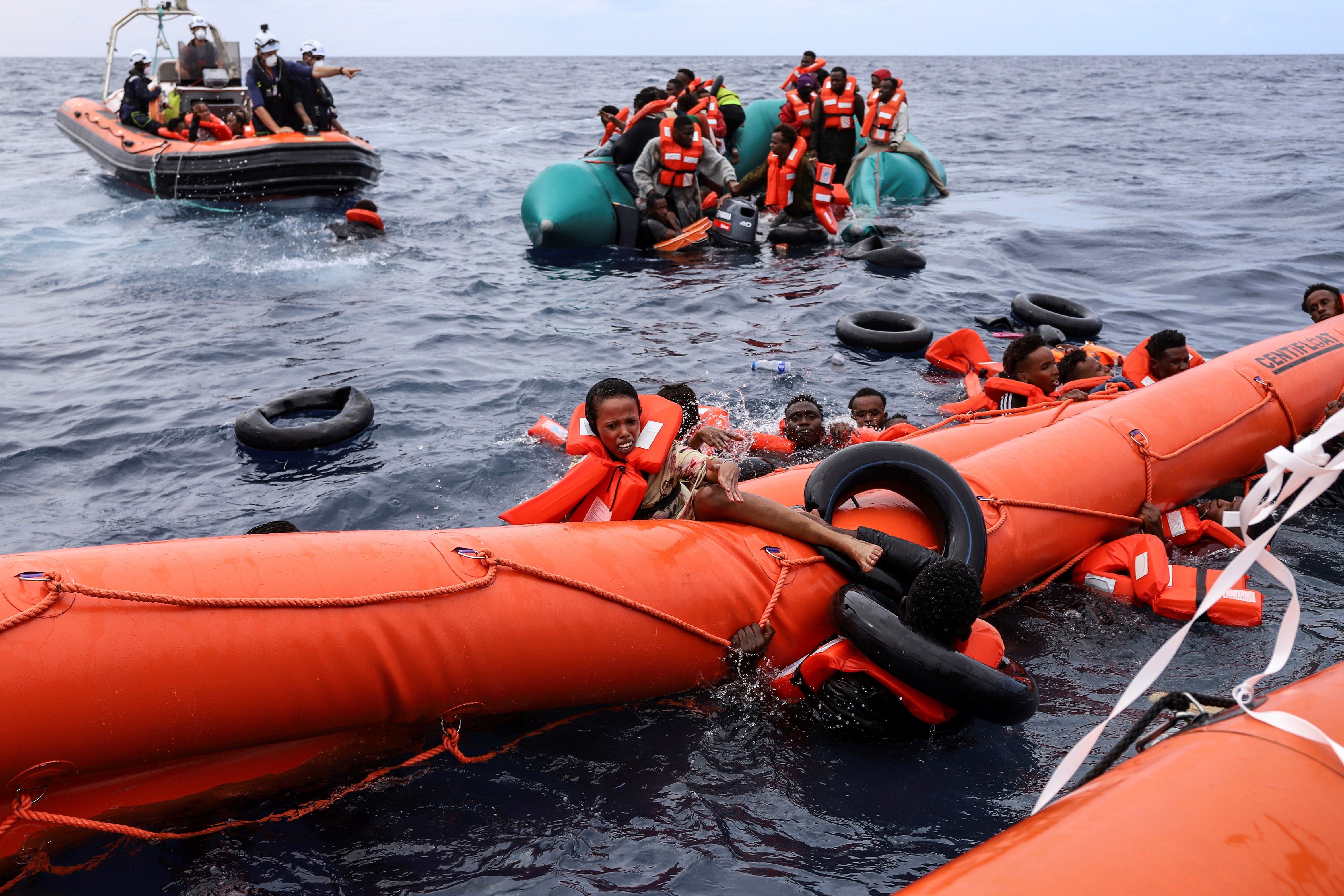 Migrants aboard a rubber boat end up in the water while others cling on to a centifloat before being rescued by a team of the Sea Watch-3, around 35 miles away from Libya, October 18, 2021 (AP)
