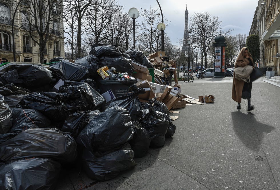 A woman walks past an uncollected garbage pile in Paris, Monday, March 20, 2023.