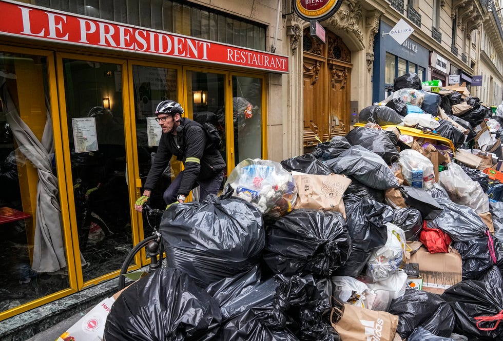 A cyclist rides past an uncollected garbage pile next to the cafe "The President" in Paris, Tuesday, March 21, 2023.