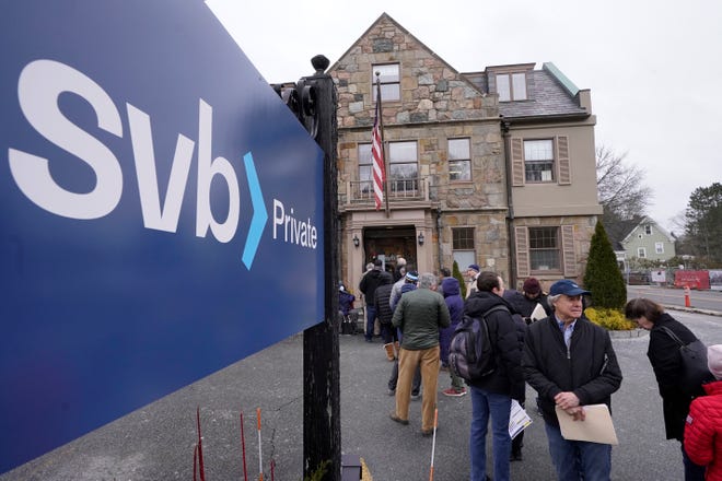 Customers and bystanders form a line outside a Silicon Valley Bank branch location, Monday, March 13, 2023, in Wellesley, Mass. The sudden crisis in the U.S. banking industry is sure to cause some tightening of lending and credit and a slowdown in the pace of borrowing and spending.