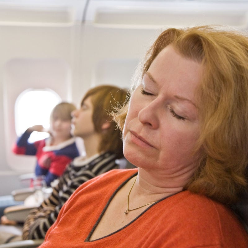 A woman in a red shirt sleeps on an airplane next to two young passengers