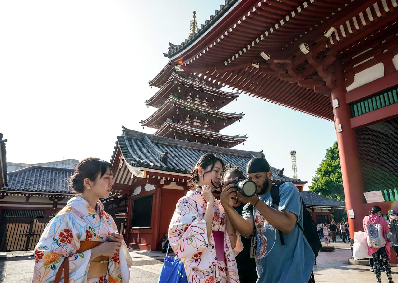 Tourists take pictures with women in traditional dresses outside a Japanese temple.