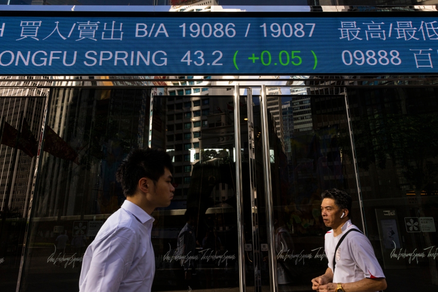 Pedestrians pass by the Hong Kong Stock Exchange electronic screen in Hong Kong, Thursday, June 29, 2023. Asian stock markets were mixed Thursday after leaders of major central banks said they need to keep interest rates high to fight persistent inflation despite fears that might tip the global economy into recession. (AP Photo/Louise Delmotte)