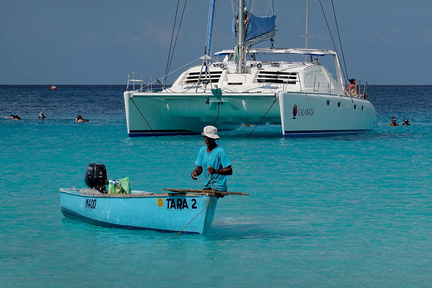 A man fishes from a small boat in front of a larger yacht in the turquoise waters off Bridgetown, Barbados, in 2021.