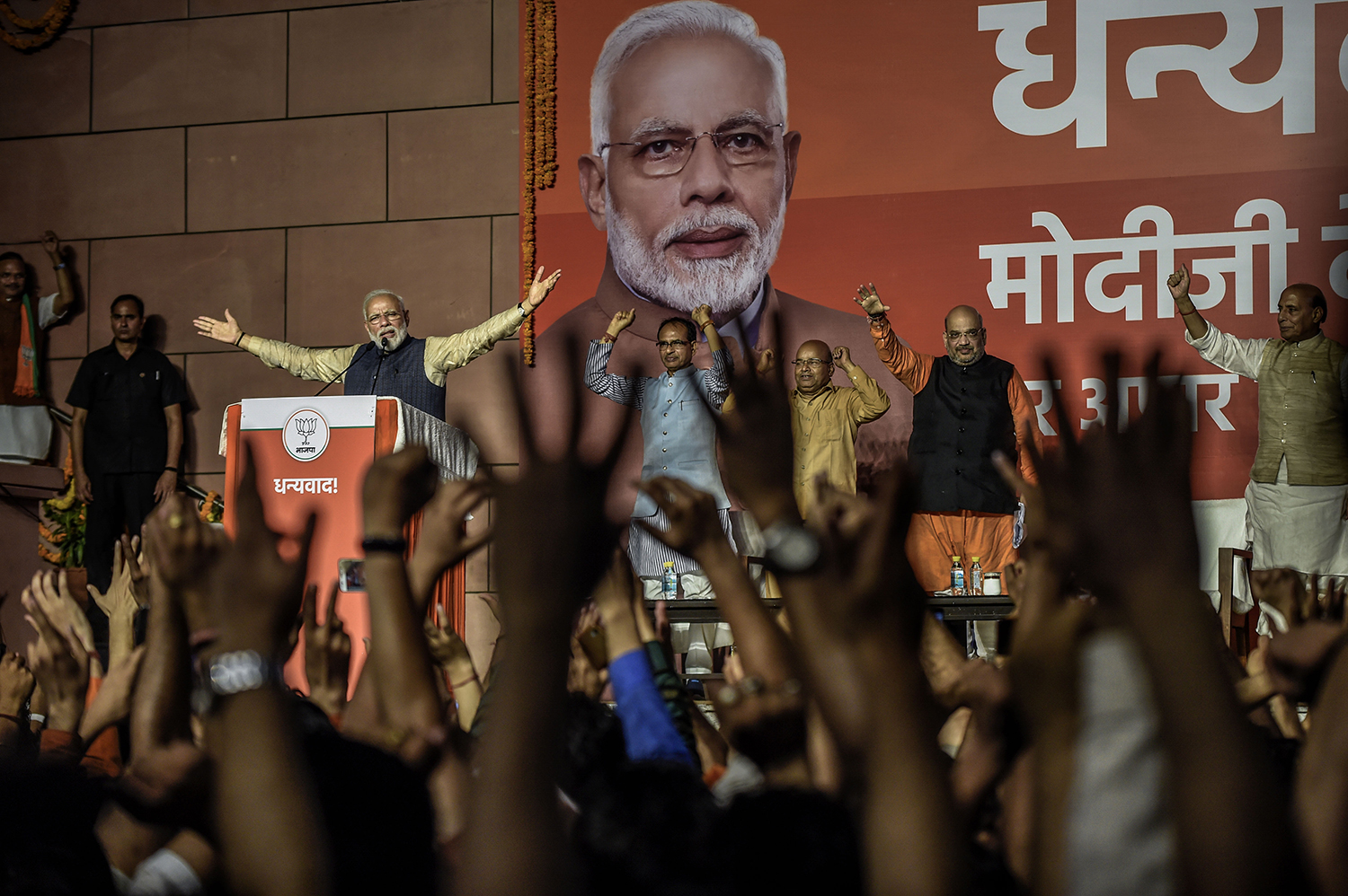 Indian Prime Minister Narendra Modi gestures with his arms wide under a portrait of himself as he addresses a crowd of victorious party workers with their arms raised at the Bharatiya Janata Party headquarters in New Delhi in 2019.