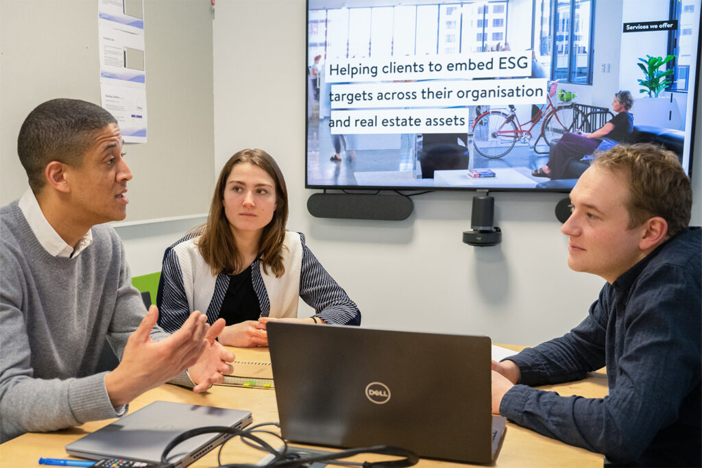 Young engineers from Buro Happold's Berlin office discuss a ESG strategy in an office environment with laptops open on the table in front of them.