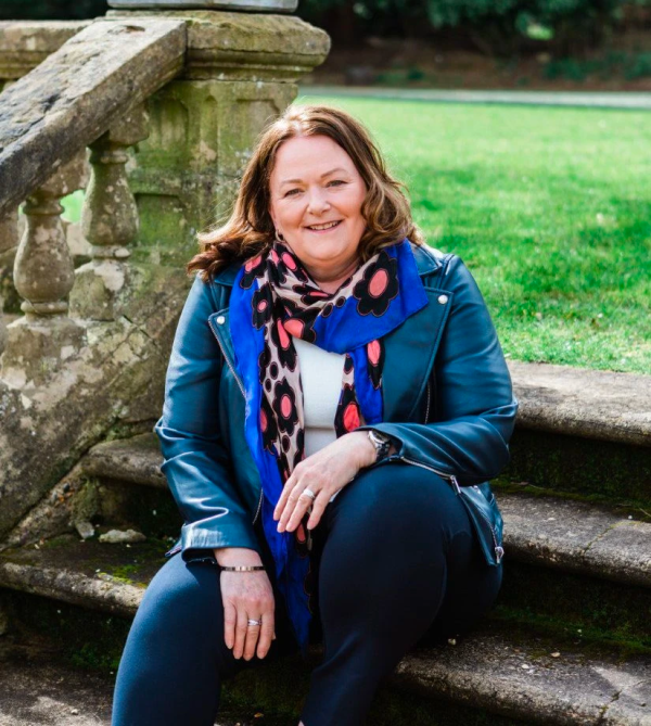 Alison sitting on the steps of a garden, looking to camera and smiling