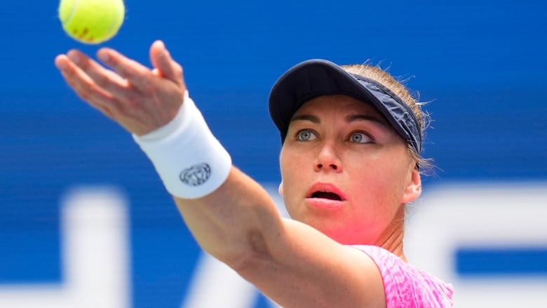 Russian female tennis player releases ball from her left hand while preparing to serve during a match.