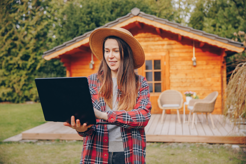 Image of a girl holding her laptop in the garden in front of the shed