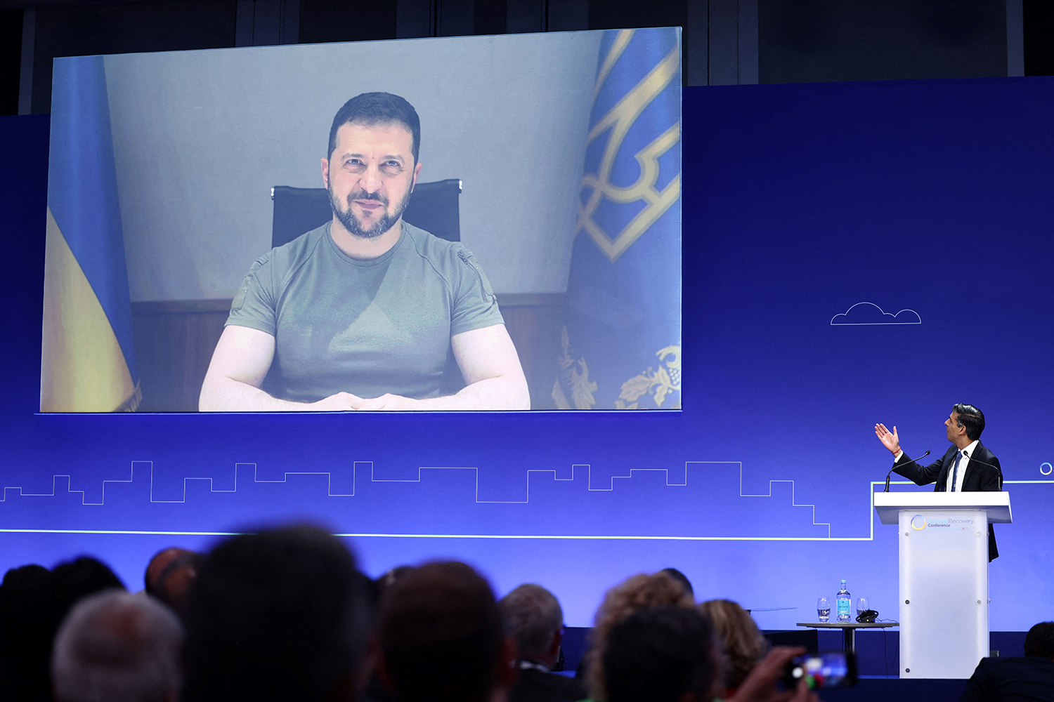 Ukraine's President Volodymyr Zelensky appears on a screen above a stage during the Ukraine Recovery Conference