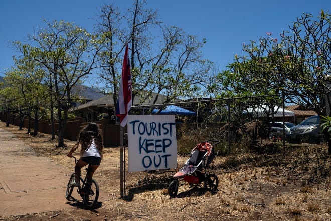 A girl rides her bike past a sign that says "Tourist Keep Out," in Lahaina, Hawaii, Thursday, Aug. 17, 2023. Long before a wildfire blasted through the island of Maui the week before, there was tension between Hawaii's longtime residents and the visitors some islanders resent for turning their beaches, mountains and communities into playgrounds. But that tension is building in the aftermath of the deadliest U.S. wildfire in more than a century. (AP Photo/Jae C. Hong)