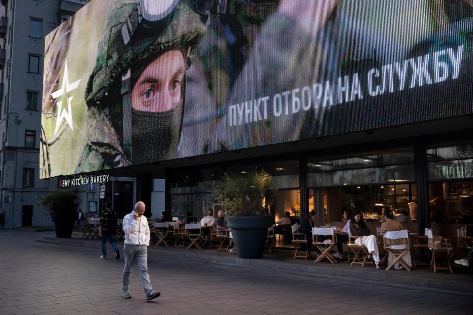 A man walks past a street side cafe with an army recruiting screen calling for a contract for service,  in the Russian armed forces in the center of Moscow, Russia (AP)