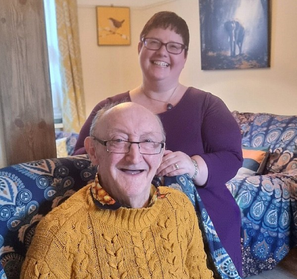 Helen stands behind her husband Ian in their sitting room