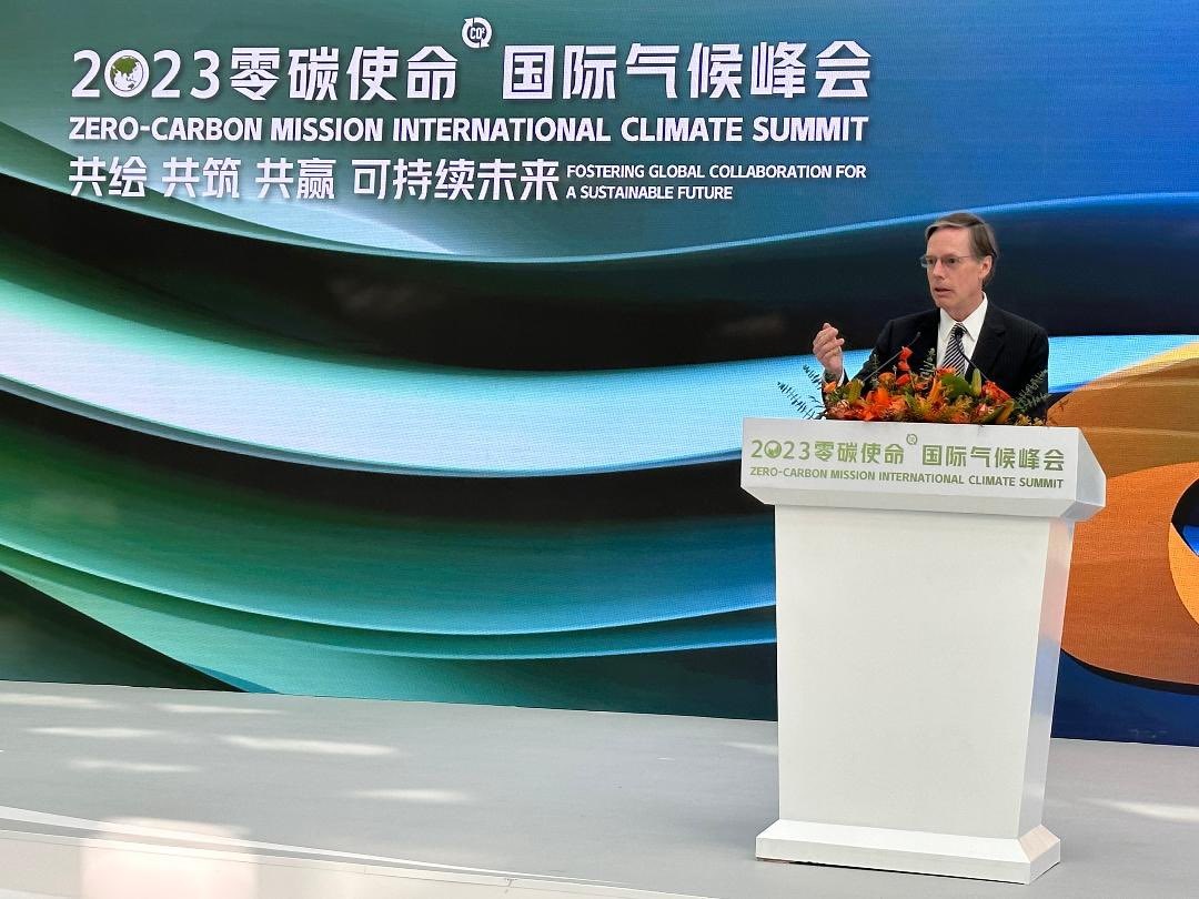 Ambassador Burns speaking behind a white podium on a stage at the 2023 Zero-Caron Mission International Climate Summit.