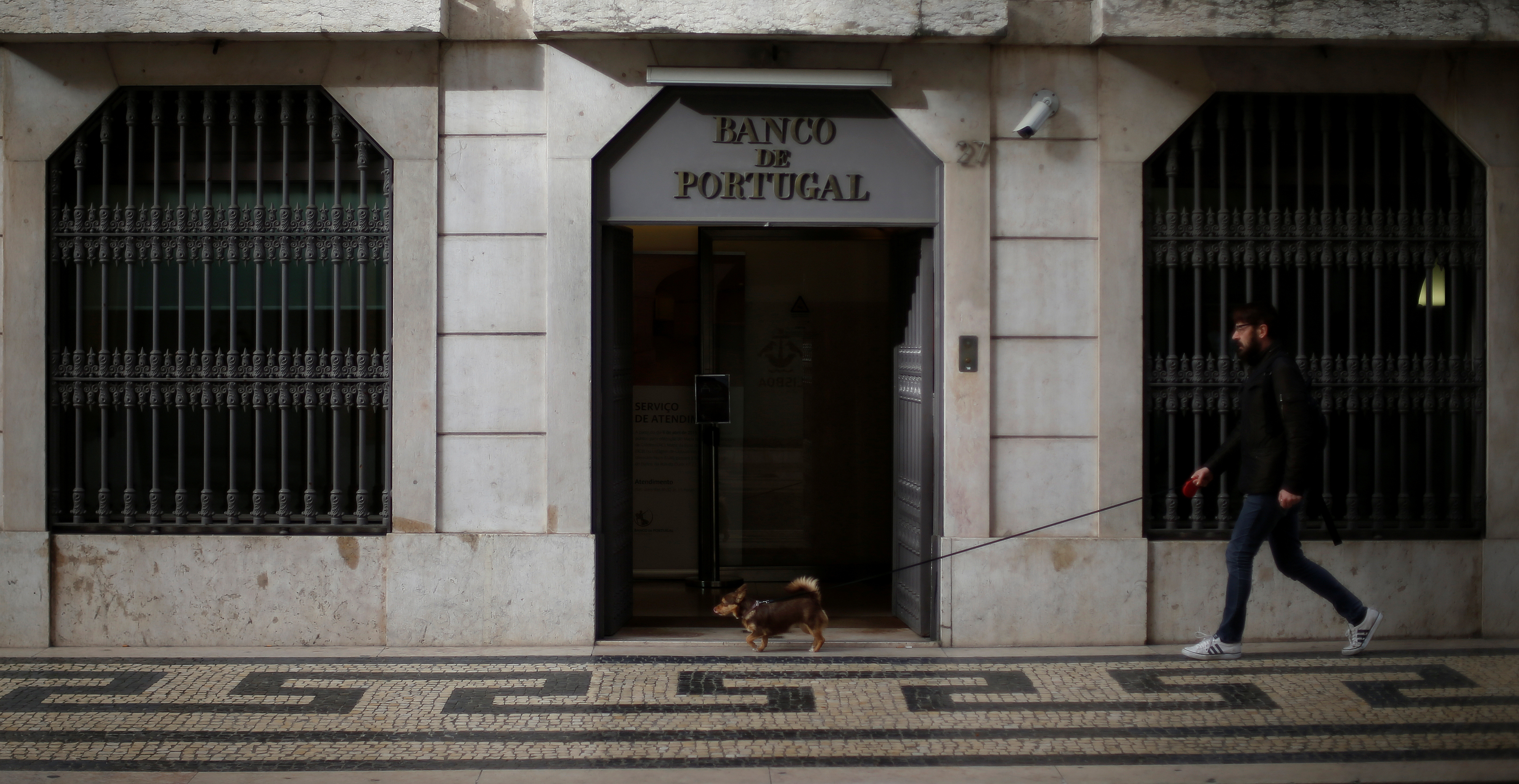 A man walks with his dog outside Bank of Portugal in downtown Lisbon