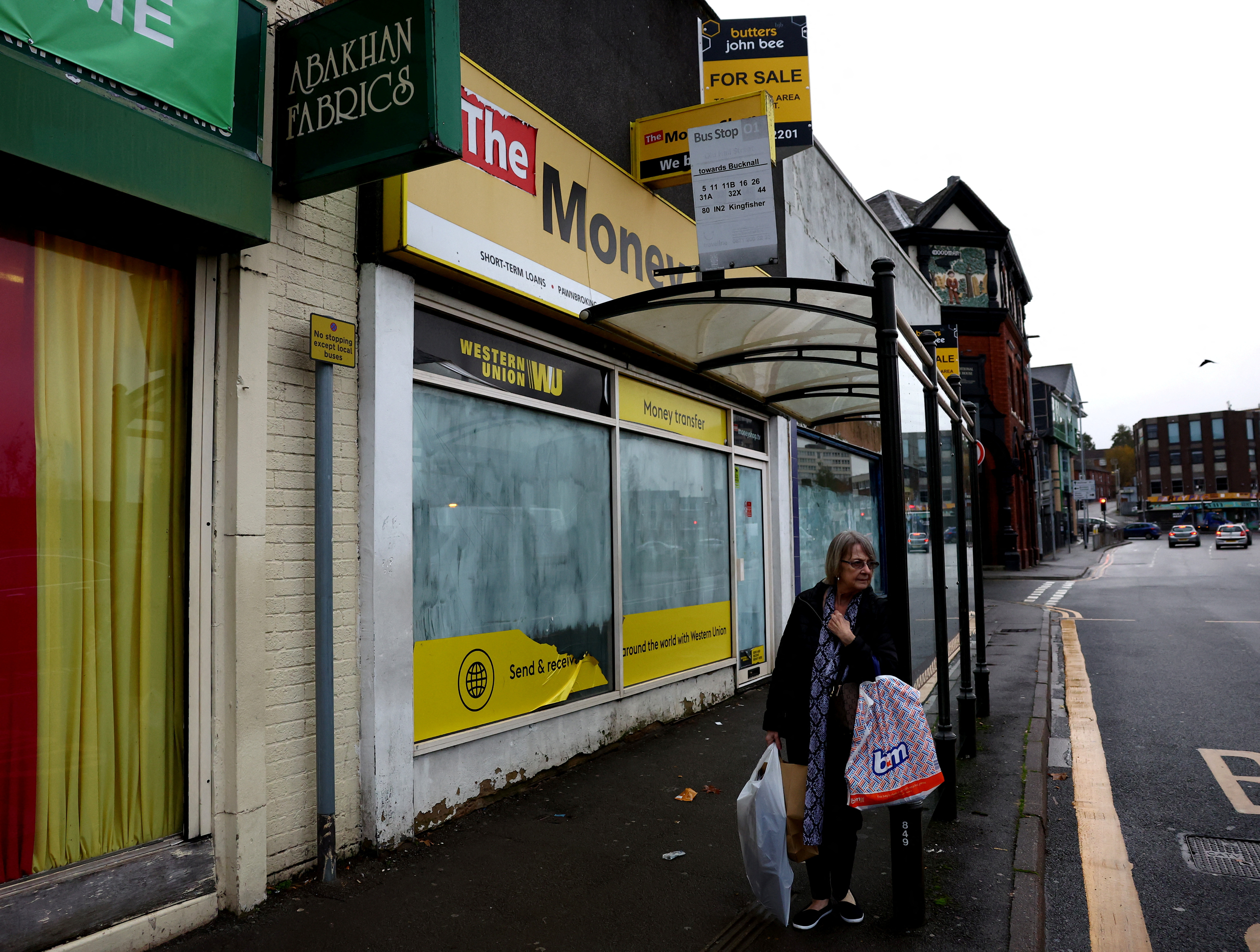 A woman with shopping bags waits for a bus