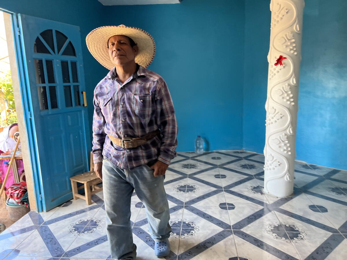 A man in a wide-brimmed hat stands in a room painted light blue. 