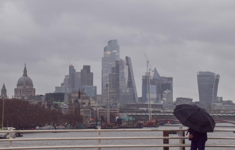 FTSE London, UK. 27th December 2023. A pedestrian walks across Waterloo Bridge past the City of London skyline, the capital's financial district, amidst strong winds and rain as Storm Gerrit hits the UK. Credit: Vuk Valcic/Alamy Live News