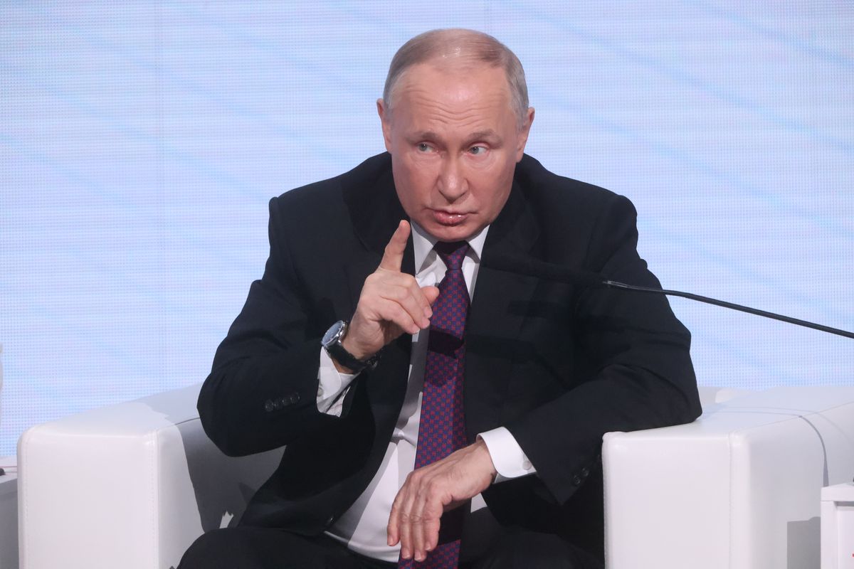 Russian President Vladimir Putin sitting on a stage with a microphone.