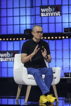 Changpeng Zhao, Binance founder, sits on a white chair with a Web Summit logo in the background.