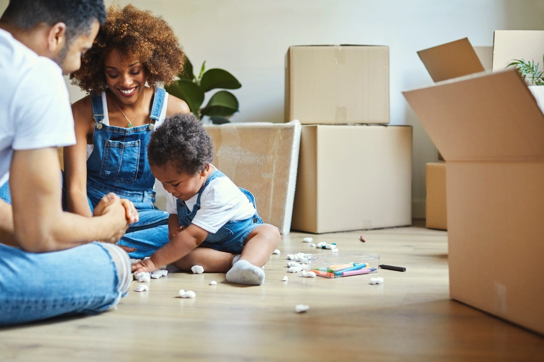 Young parents and baby sitting in new house surrounded by moving boxes