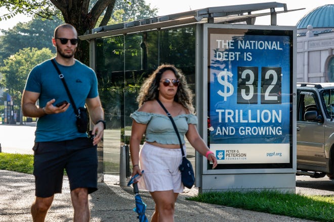 WASHINGTON, DC - JULY 06: Pedestrians walk past a poster and electronic billboard displayed at Independence Ave and 9th St's SW that displays the current U.S. National debt per person and as a nation at 32 Trillion dollars on July 06, 2023 in Washington, DC.
