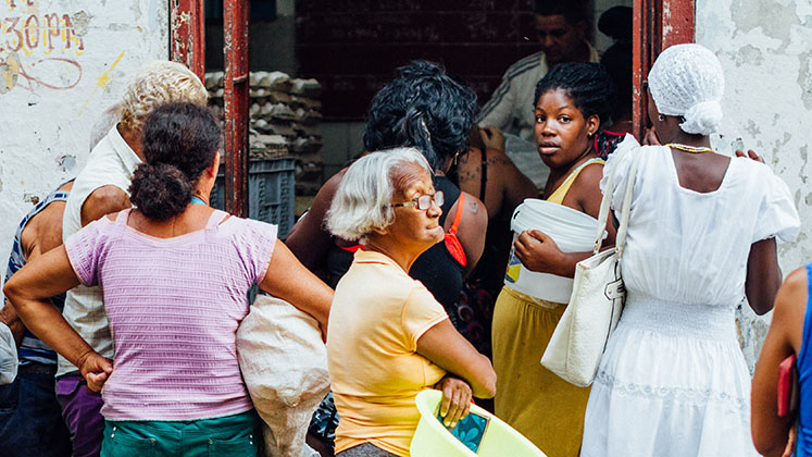 A group of women in Havana, Cuba, wait around the entrance of a food dispensary