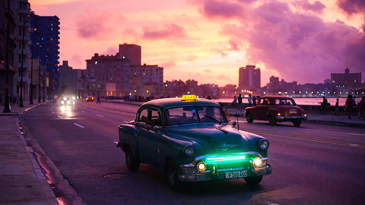 A taxi rolls through Havana at twilight