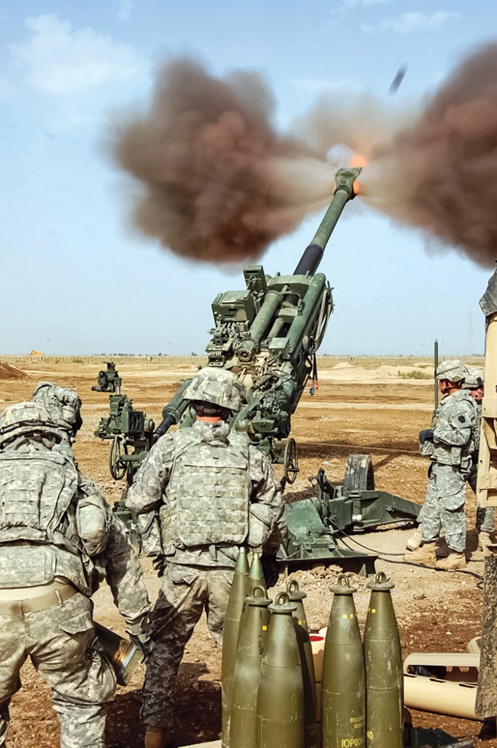 A howitzer being fired by a team of five soldiers.