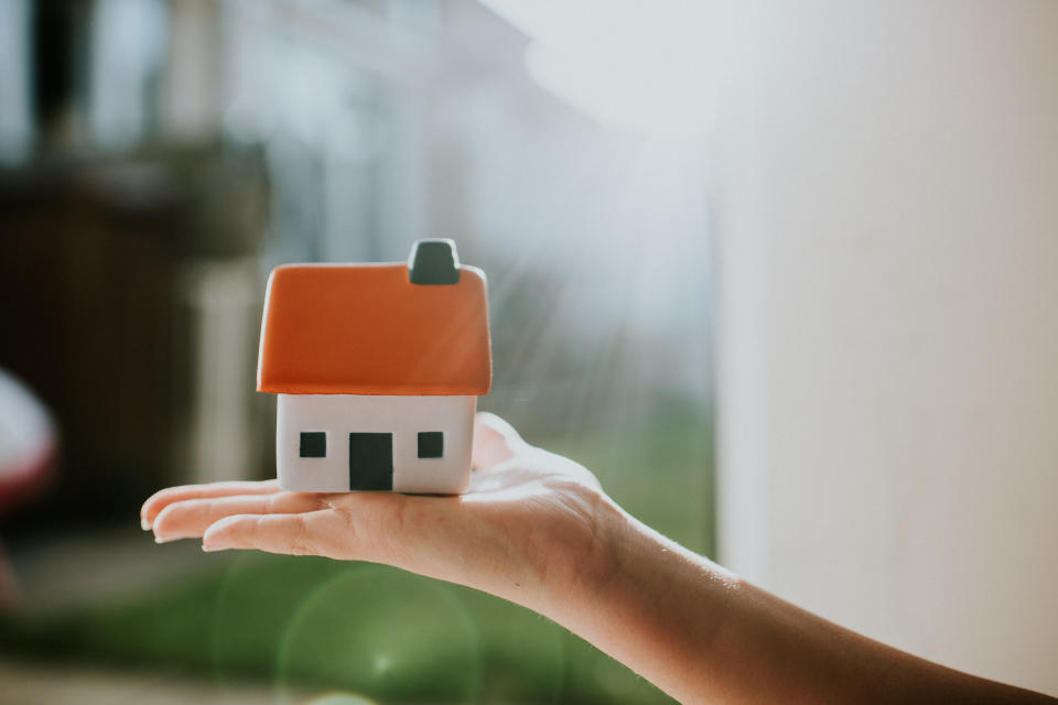 Hand holding a little house with an orange roof. Conceptual image with space for copy.