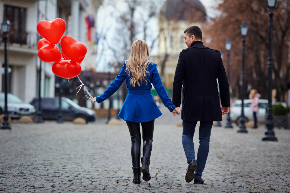 A young couple in a coat are holding a balloons heart in the city street. Valentine's Day. money