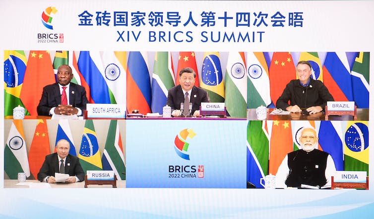 Under a banner with Chinese letter and 'XIV BRICS SUMMIT' five screens show the face of five world leaders in front of flags.