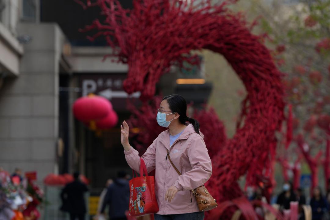 A woman reacts near a dragon sculpture outside a restaurant in Beijing, Tuesday, April 9, 2024. China's Finance Ministry has denounced a report by Fitch Ratings that kept its sovereign debt rated at A+ but downgraded its outlook to negative, saying in a statement that China's deficit is at a moderate and reasonable level and risks are under control. (AP Photo/Ng Han Guan)