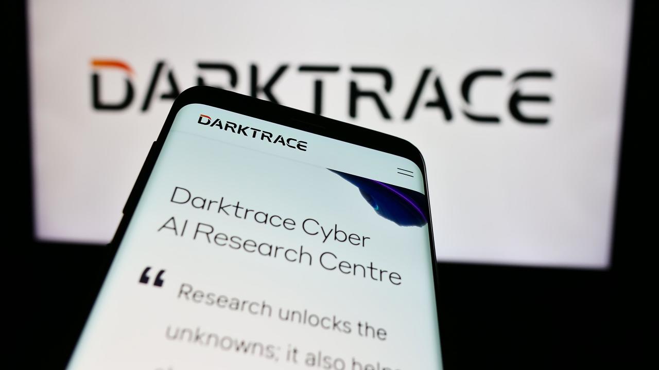 Mobile phone with website of British cyber security company Darktrace plc in front of business logo. Focus on top-left of phone display.