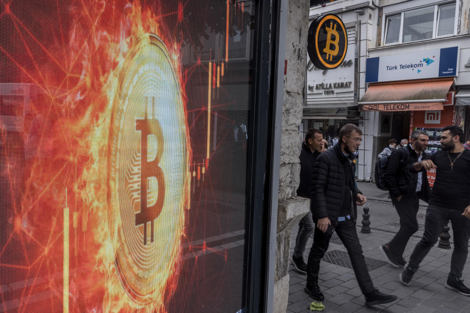 People walk past a Bitcoin symbol at the entrance of a cryptocurrency exchange office