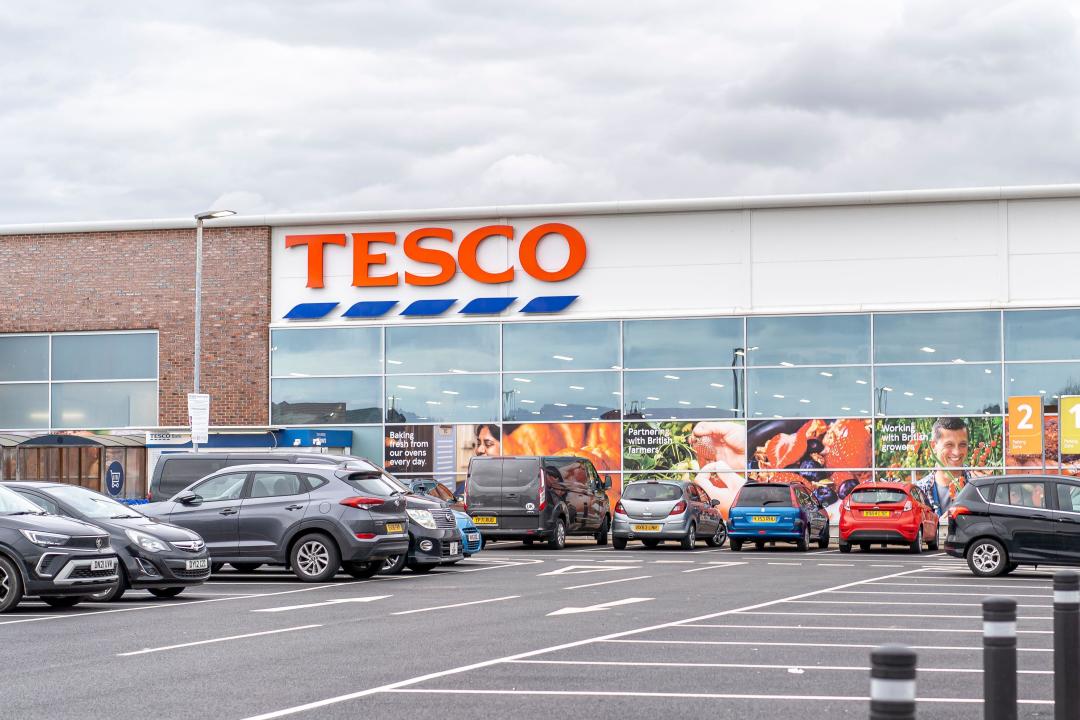 Exterior view of a UK Tesco superstore (supermarket) with parked cars in the outdoor car park.