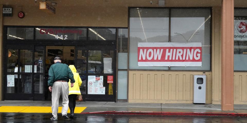 People walk by a now hiring sign posted in front of a CVS store