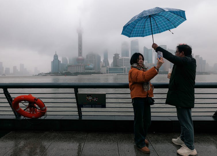 Two tourists taking pictures in front of the Shanghai skyline in the rain
