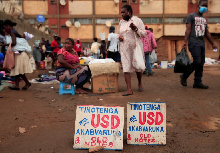 People walk past a money-changers sign at a market in Harare