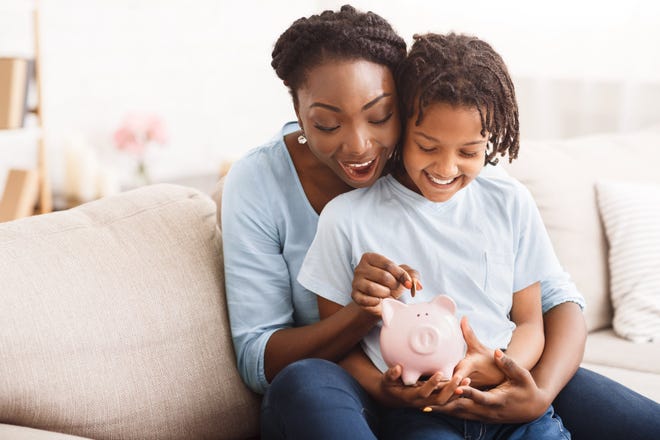 An adult and child put coins into a piggy bank.