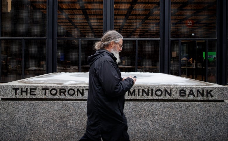 A man walks past a sign that says 'The Toronto Dominion Bank." 