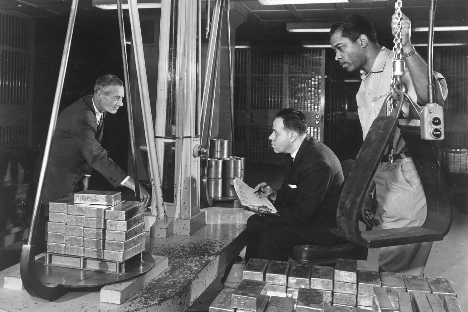 A historic image of three men in the vault of a bank weighing gold bars.