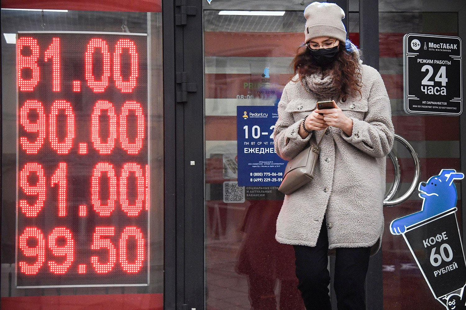 A woman looks at her phone as she walks past a currency exchange office in central Moscow.