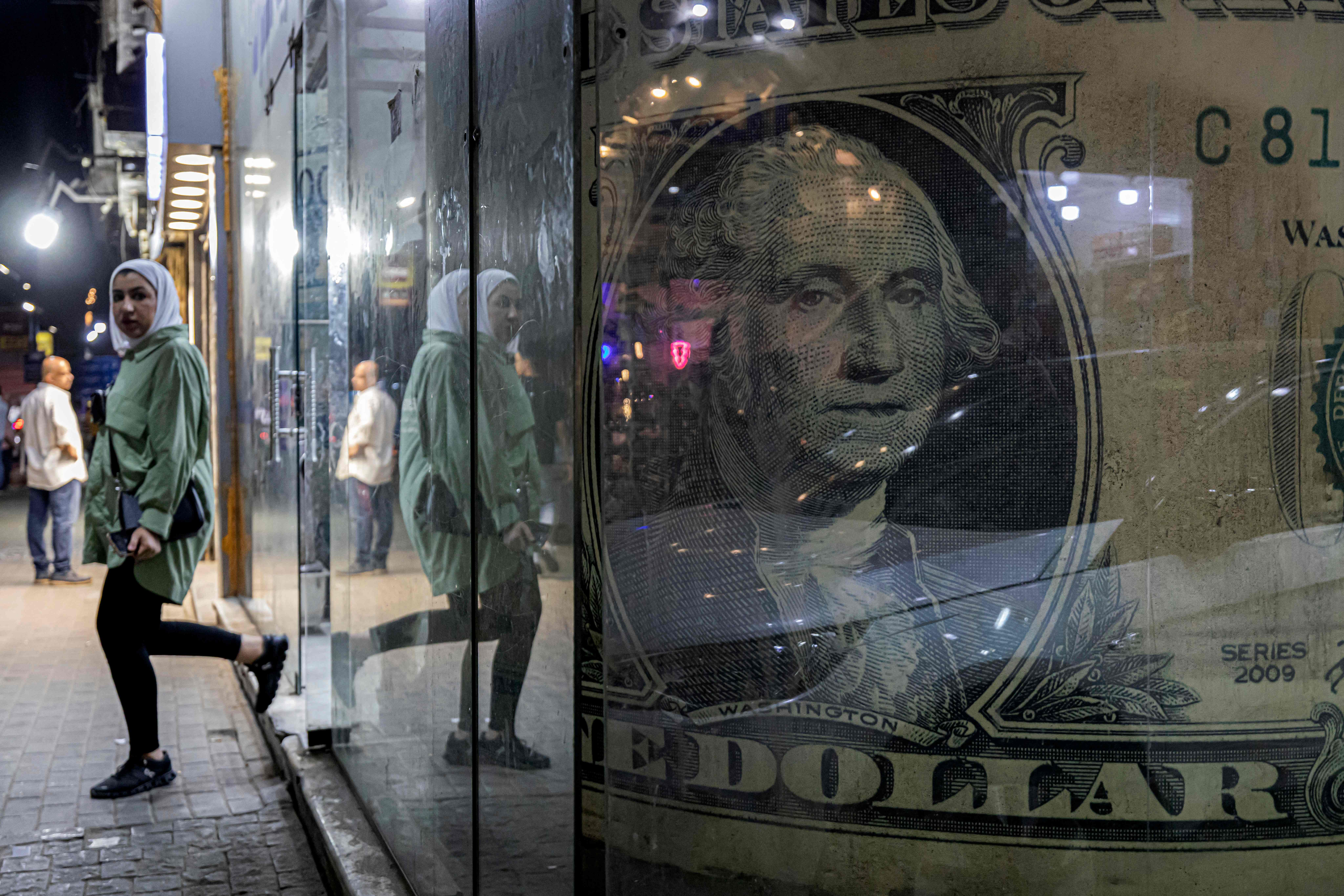 A woman walks out of a currency exchange shop in Cairo. A giant $1 bill can be seen inside the window of the shop.