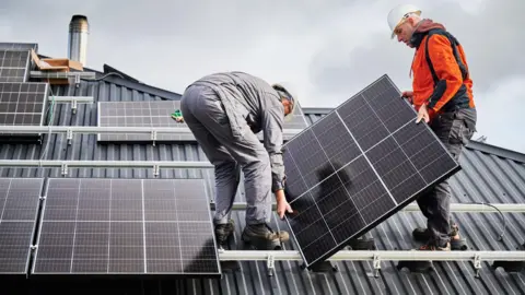 Getty Images Two men work to attach solar panels to a roof